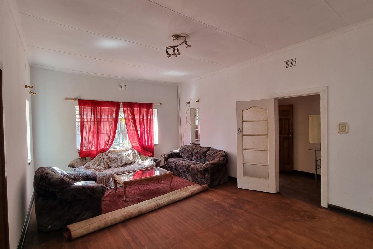 A spacious living room featuring original wooden flooring and natural light, offering a blank canvas for renovation and modern interior design updates.