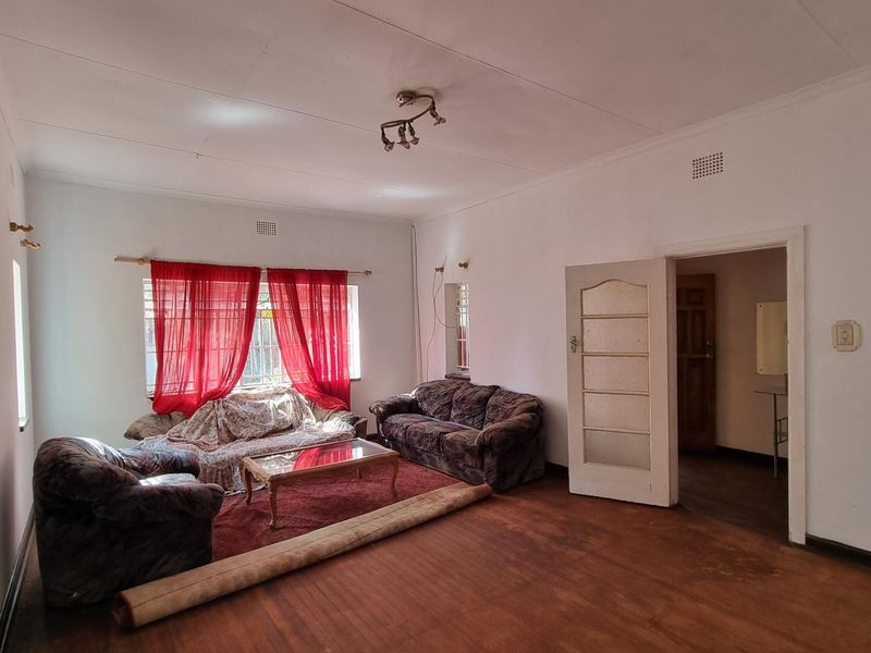 A spacious living room featuring original wooden flooring and natural light, offering a blank canvas for renovation and modern interior design updates.