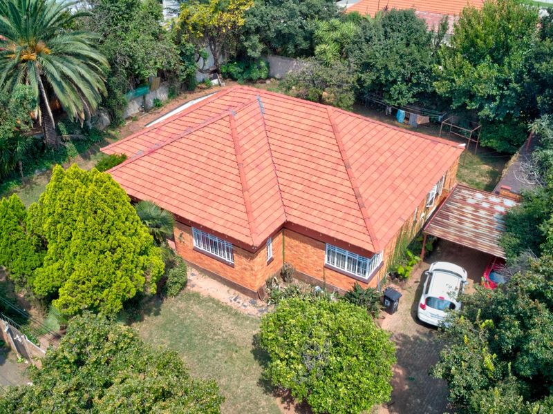 Aerial view of a brick house featuring a tiled roof, established garden, and a carport.