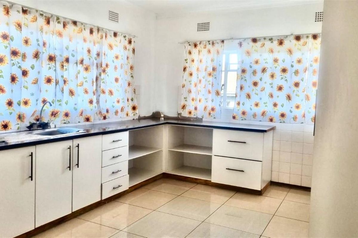 A functional kitchen featuring white cabinetry, dark countertops, a stainless steel sink, and tiled flooring with natural light from two windows.