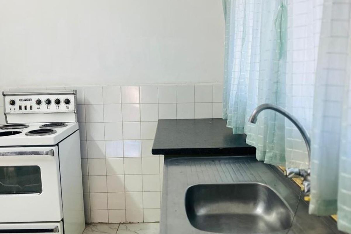 A functional kitchen area featuring a double stainless steel sink, tiled splashbacks, and a freestanding white stove.