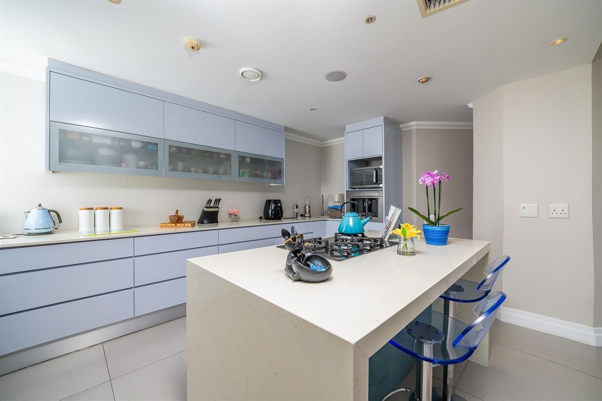 Modern kitchen featuring a central island with a built-in gas hob, sleek cabinetry, and integrated appliances, finished with stone countertops and tiled flooring.