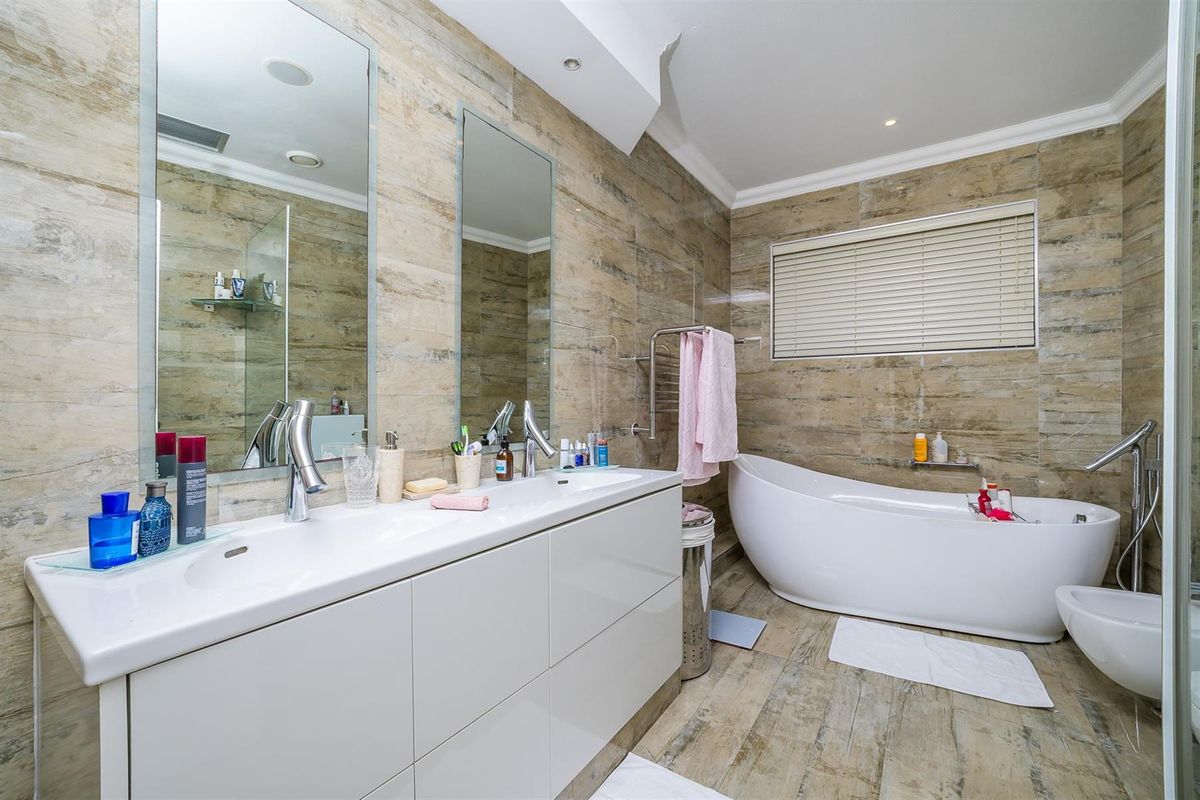 Modern bathroom featuring a double vanity with integrated sinks, a freestanding soaking tub, bidet, and floor-to-ceiling stone-look wall tiling.