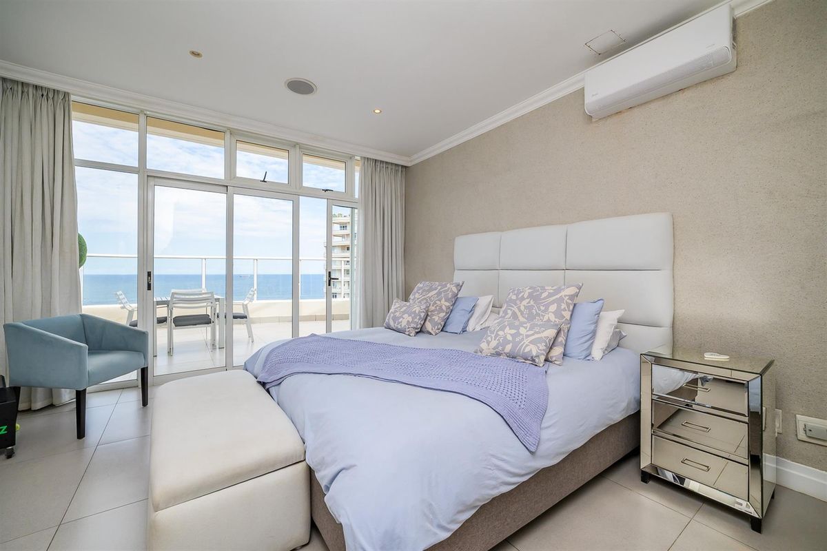 A bright bedroom featuring large sliding glass doors that open onto a private balcony with ocean views, complemented by a wall-mounted air conditioning unit.
