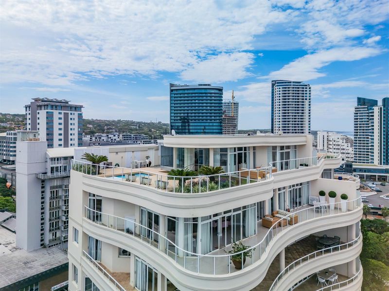 Aerial view of a modern apartment building featuring expansive curved balconies, a rooftop terrace with a pool, and contemporary architectural design.