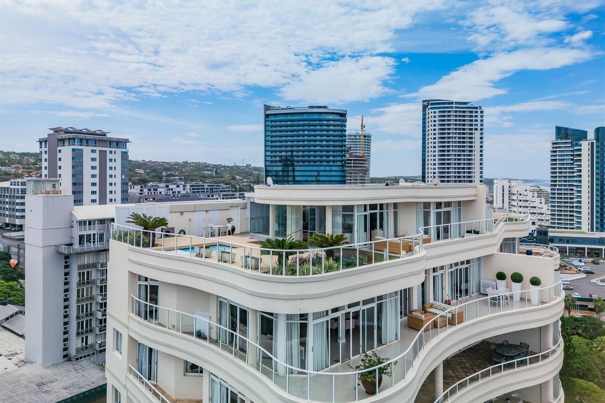 Aerial view of a modern apartment building featuring expansive curved balconies, a rooftop terrace with a pool, and contemporary architectural design.
