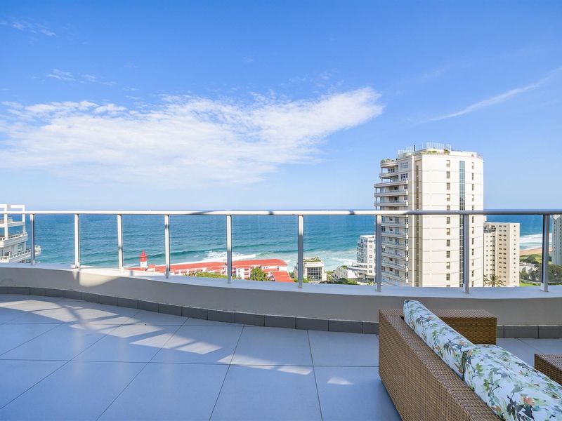 Spacious balcony featuring modern tiled flooring and a sleek glass balustrade, offering expansive panoramic ocean and coastal views.