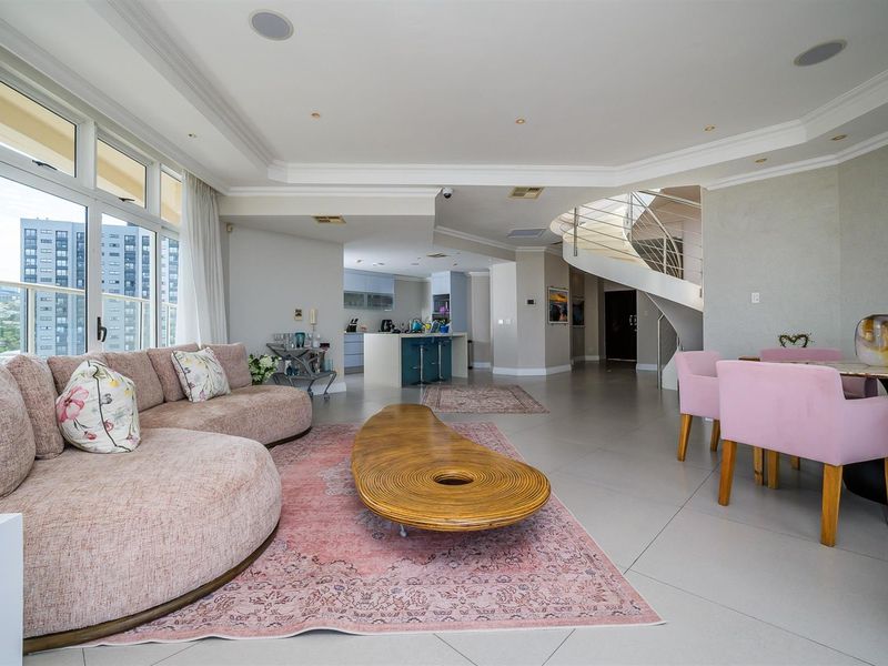 Spacious open-plan living and dining area featuring large windows, tiled flooring, recessed ceiling lighting, and a striking spiral staircase leading to the upper level.