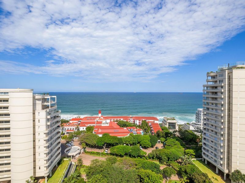 Elevated coastal view overlooking the ocean, surrounding apartment complexes, and lush green landscaped grounds.