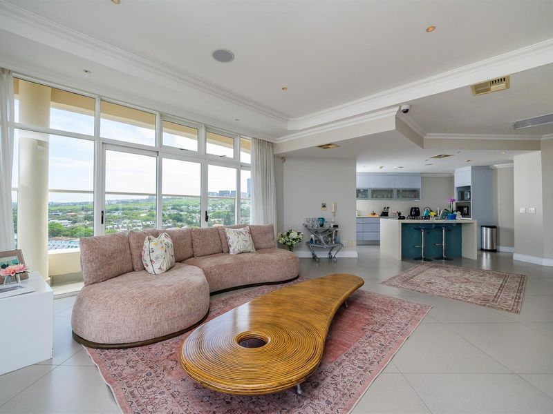Spacious open-plan living area featuring a modern kitchen with a breakfast island, tiled flooring, and large floor-to-ceiling windows offering expansive views.