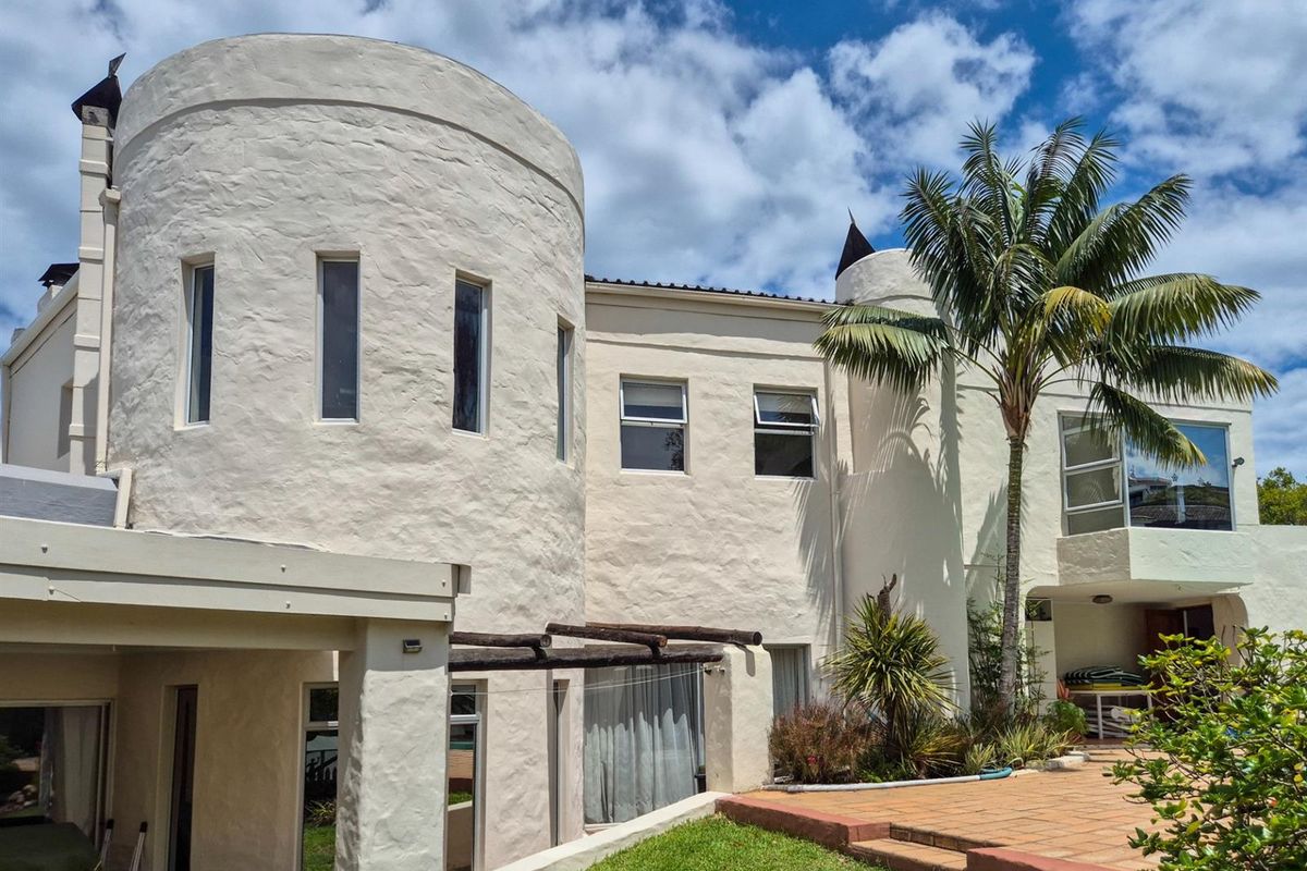 Rear view of a unique architectural home featuring a prominent circular tower, textured facade, paved patio area, and established garden landscaping.