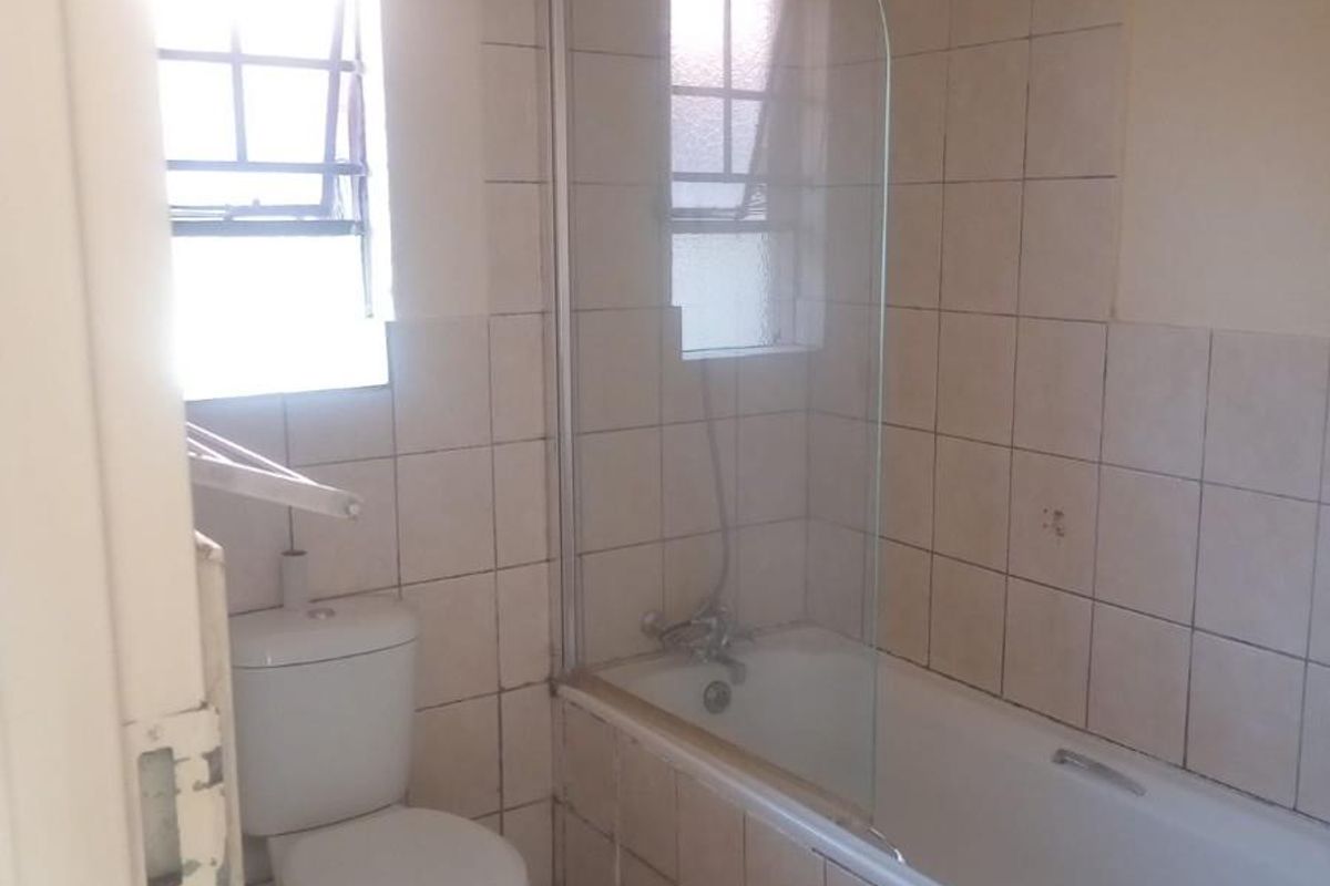 A functional bathroom featuring a standard bathtub with a glass shower screen, tiled walls, and a toilet.