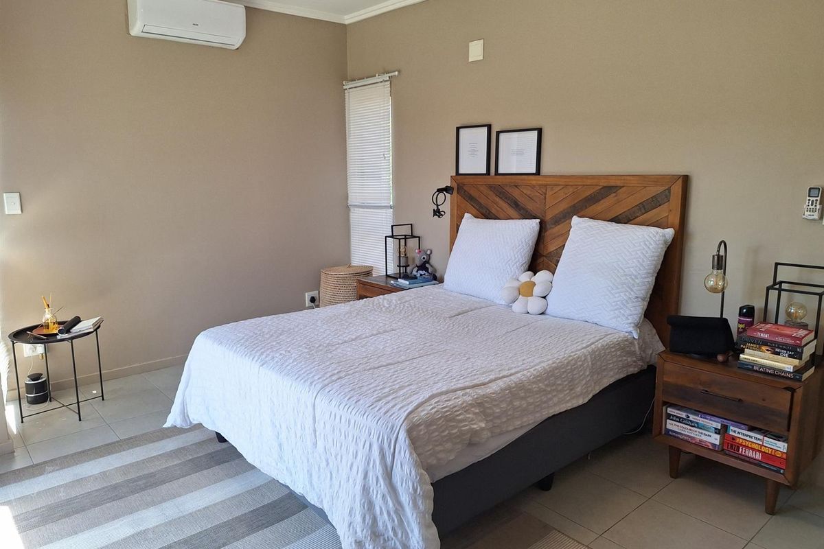 A well-maintained bedroom featuring neutral wall tones, tiled flooring, and a wall-mounted split-system air conditioning unit.