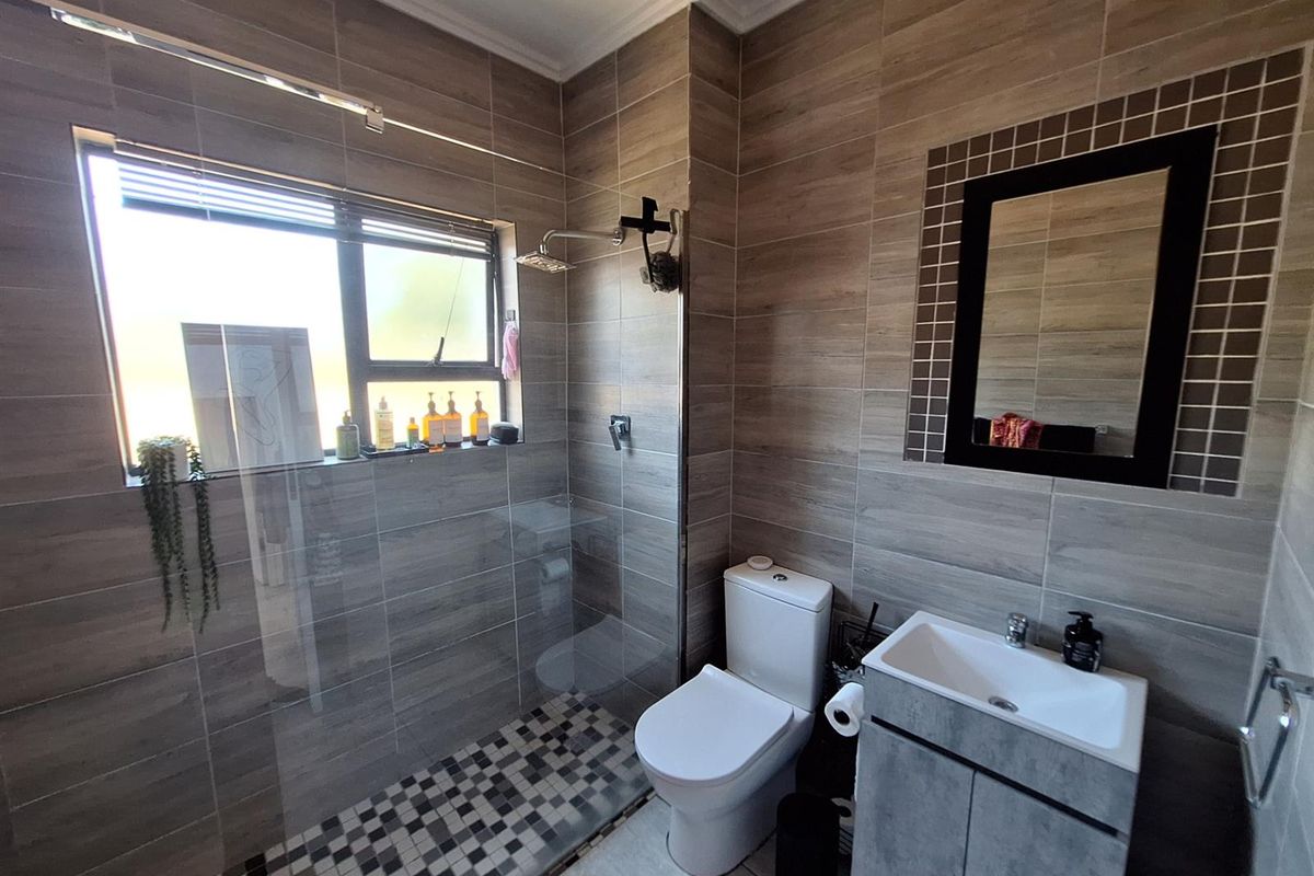 Modern bathroom featuring a walk-in shower with glass screen, vanity cabinet with basin, and contemporary wood-look wall tiling.