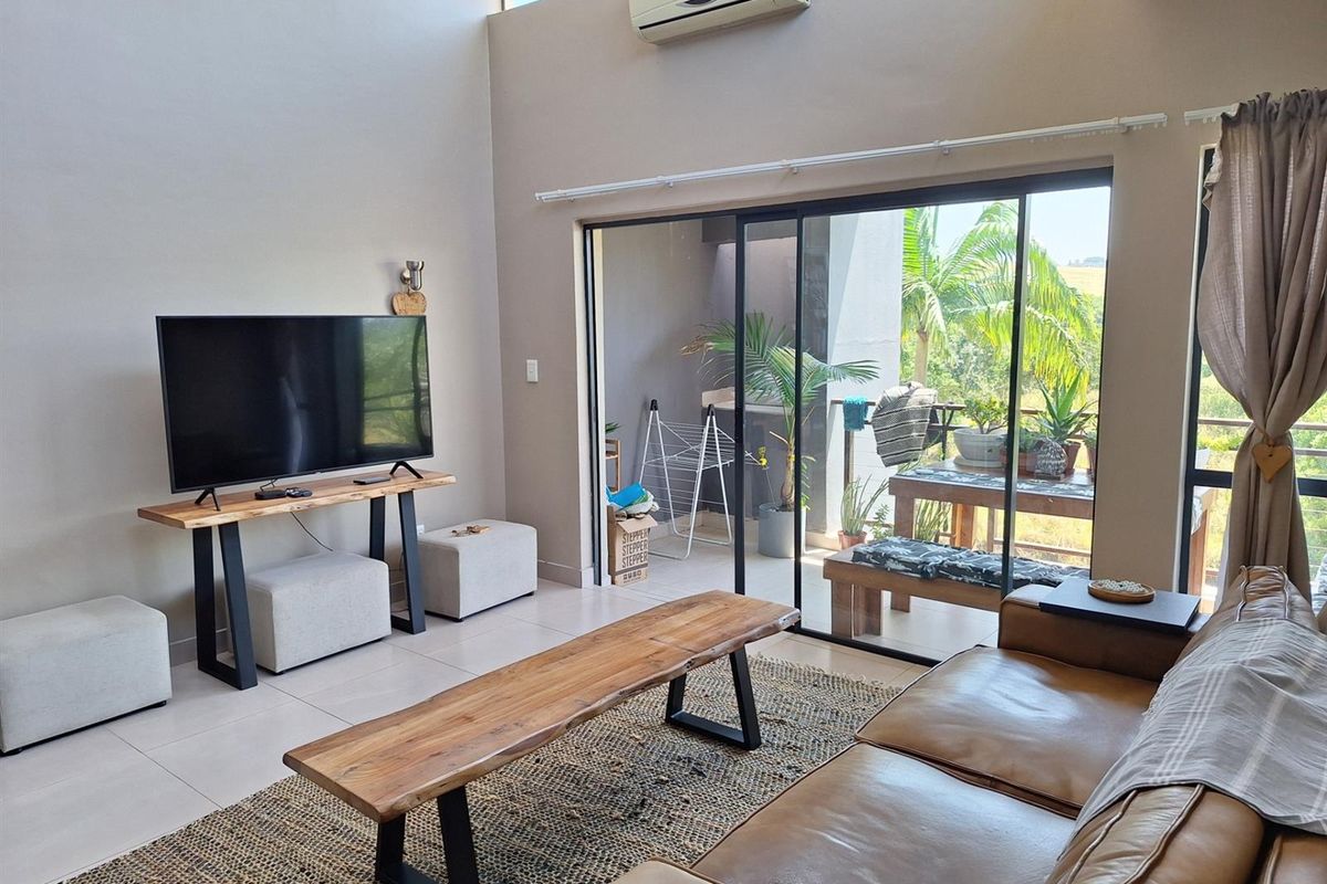 A bright living room featuring high ceilings, tiled flooring, and large sliding glass doors that provide seamless access to an outdoor patio area.