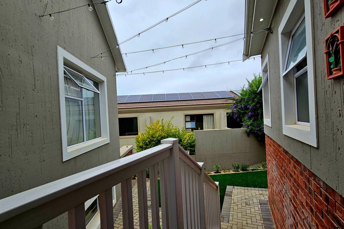 A view of the exterior side passage featuring paved walkways, a white balustrade, and solar panels installed on the roof.