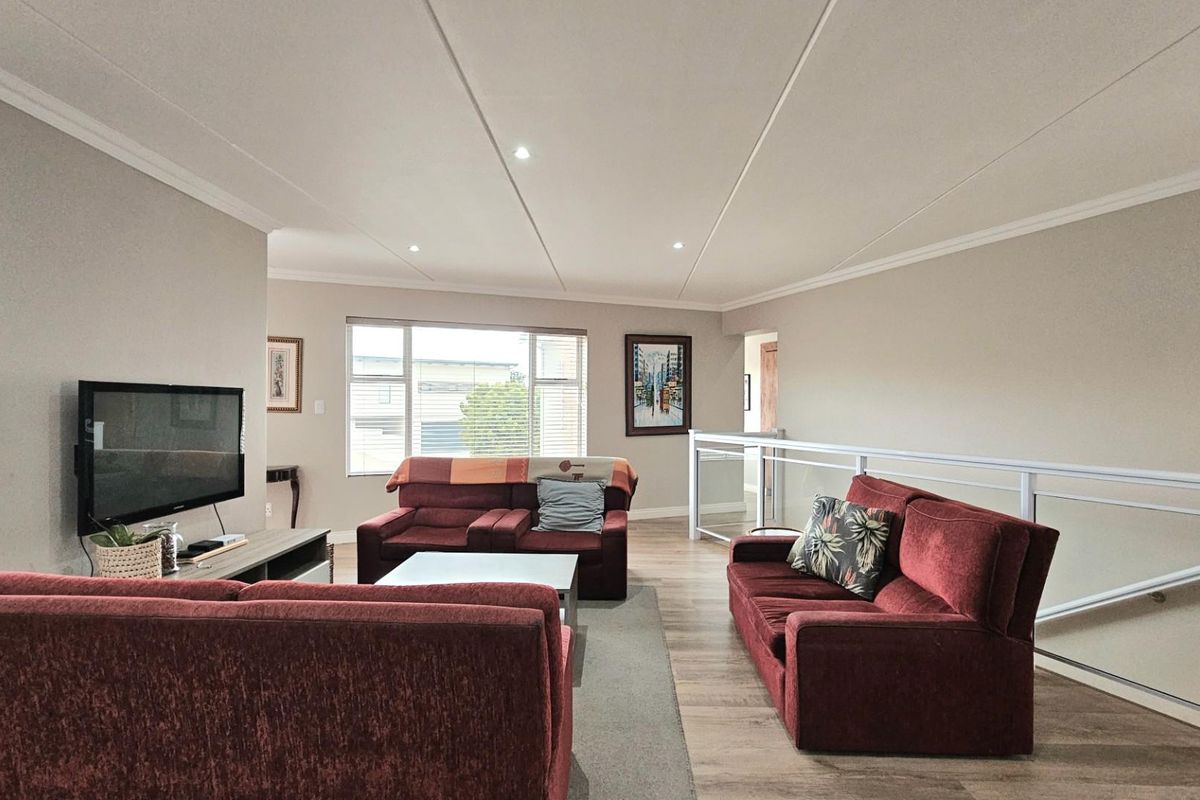 Spacious open-plan living area featuring recessed ceiling lighting, modern laminate flooring, and a glass balustrade overlooking the lower level.