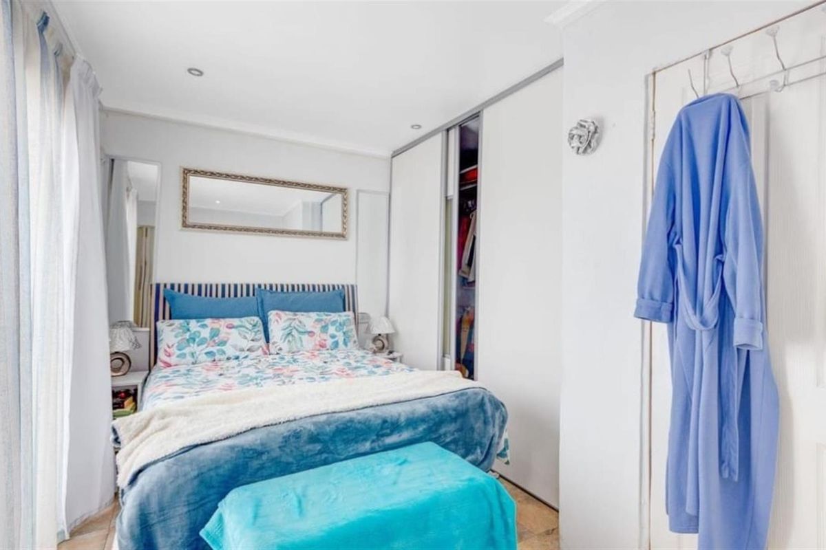 A bright bedroom featuring built-in sliding door wardrobes, recessed ceiling lighting, and tiled flooring, offering a clean and functional living space.
