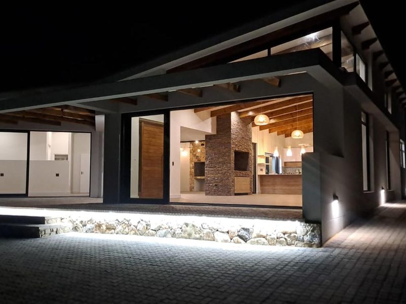 Modern architectural exterior view at night featuring a covered patio, stone cladding accents, exposed timber beams, and integrated LED lighting.
