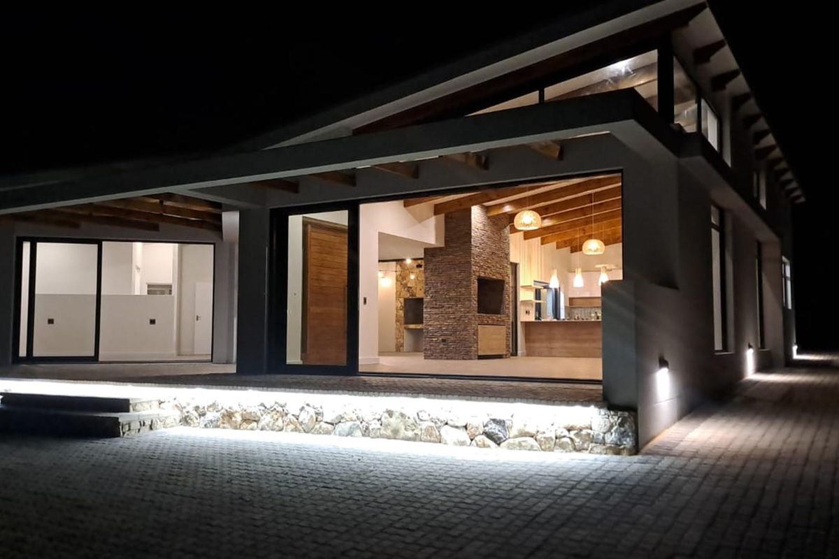Modern architectural exterior view at night featuring a covered patio, stone cladding accents, exposed timber beams, and integrated LED lighting.