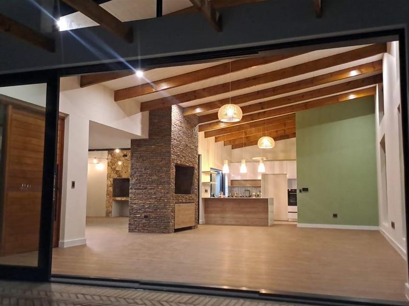 Spacious open-plan living area featuring exposed timber ceiling beams, a striking stone-clad fireplace, and a modern kitchen with integrated cabinetry.