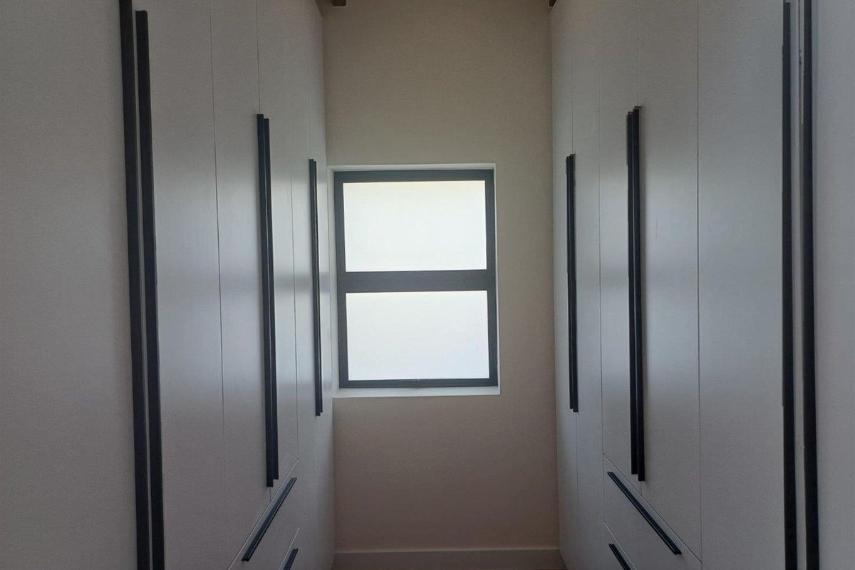 A walk-in closet or dressing area featuring floor-to-ceiling built-in cabinetry with modern handles and a central window.