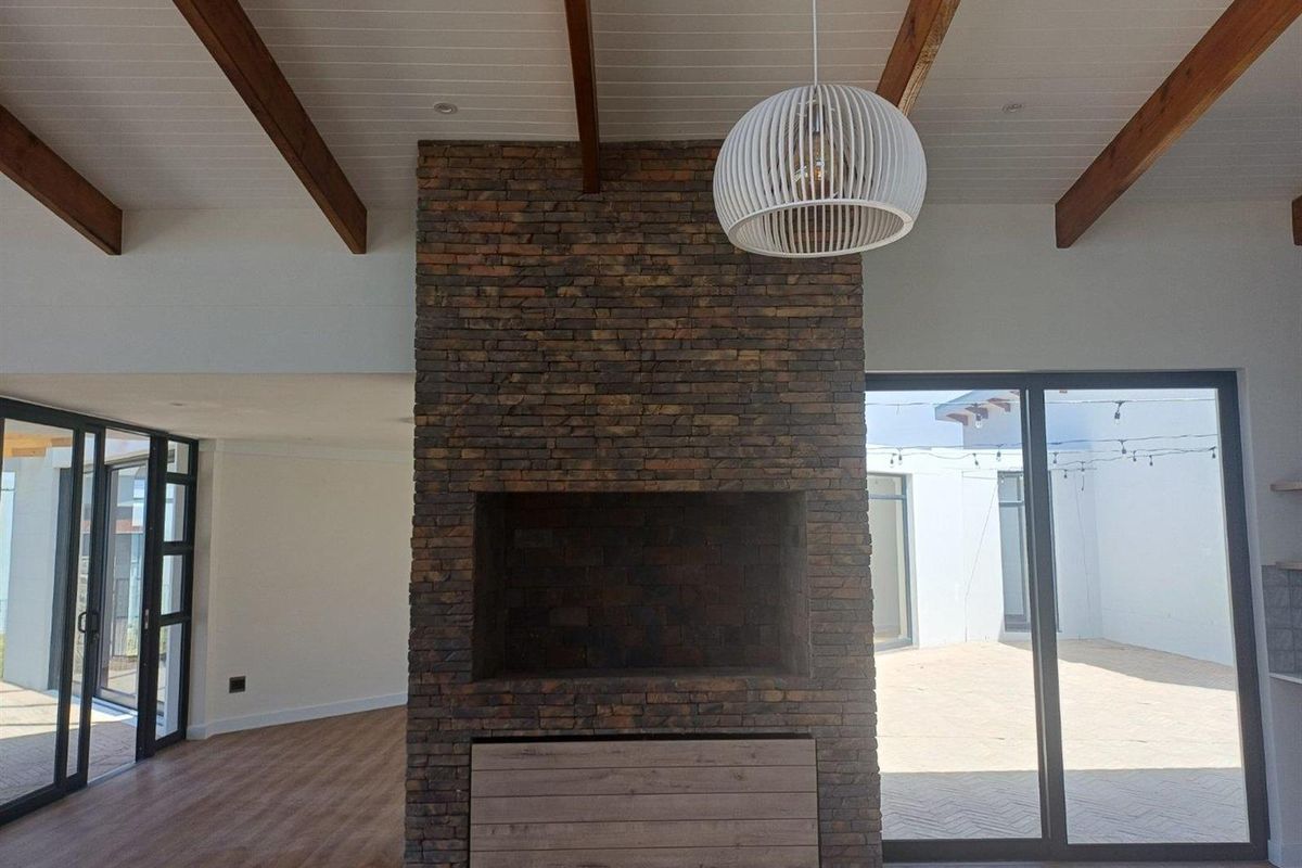 Spacious living area featuring a prominent floor-to-ceiling brick fireplace, exposed timber ceiling beams, and large sliding glass doors opening to an outdoor patio.