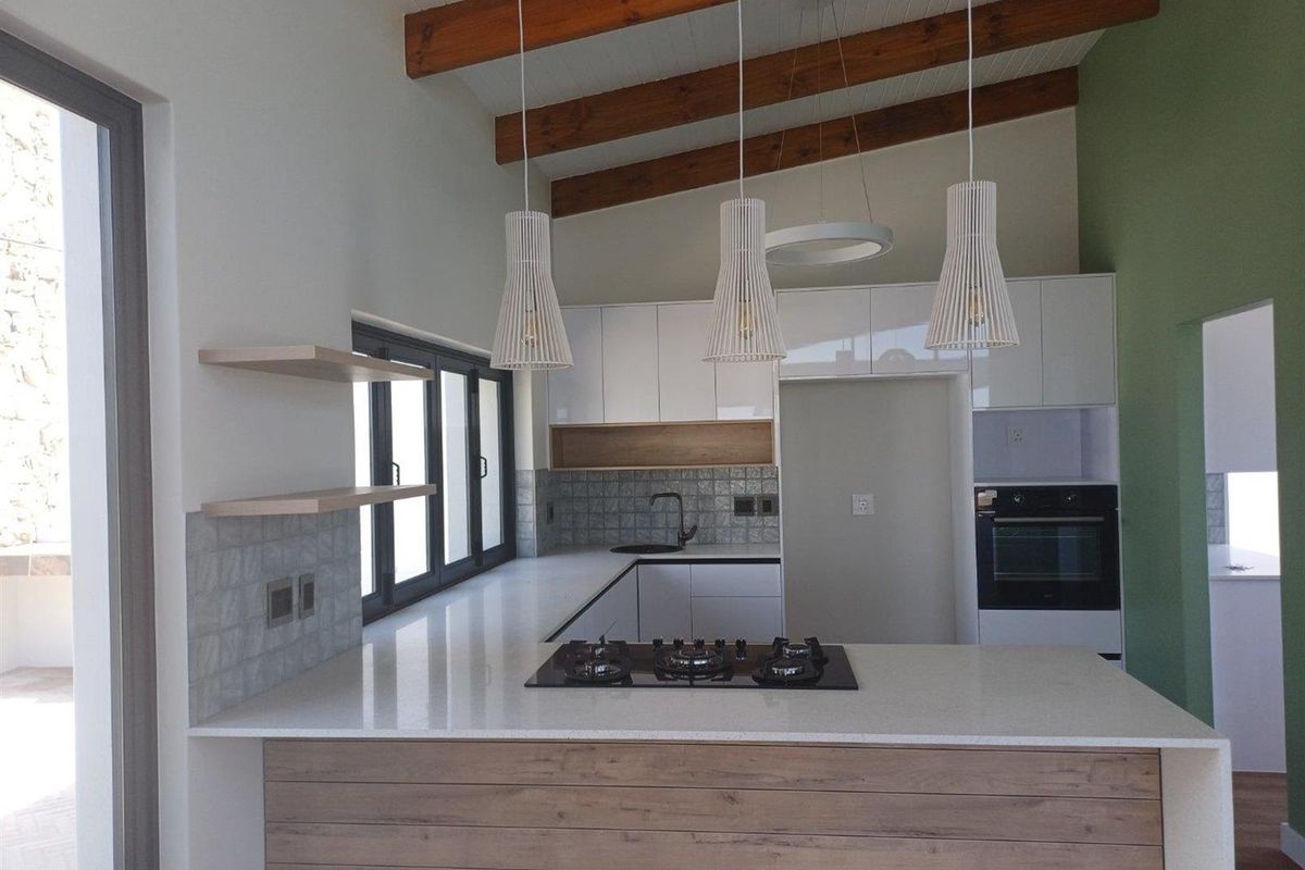 Modern kitchen featuring a central island with a built-in gas hob, sleek white cabinetry, timber ceiling beams, and a tiled backsplash.