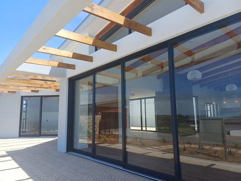 Modern patio area featuring a timber pergola, large sliding glass doors, and herringbone paved flooring, seamlessly connecting the indoor and outdoor living spaces.