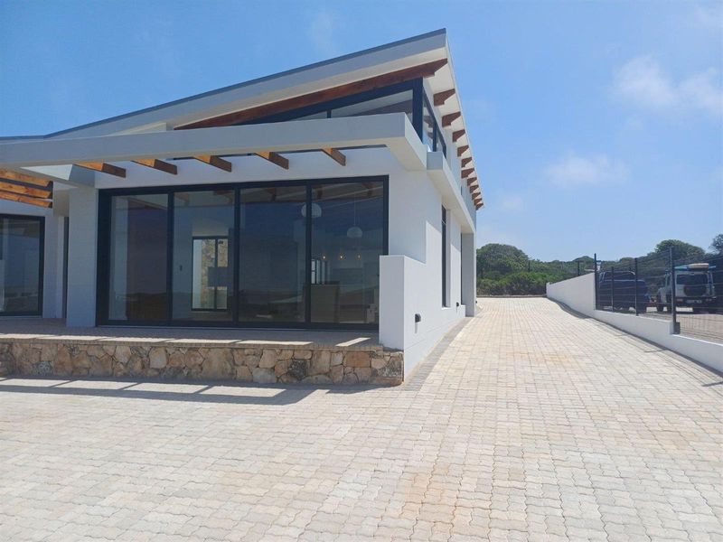 Modern exterior view of the property featuring a paved driveway, stone-clad base, and large sliding glass doors under a contemporary roof structure.