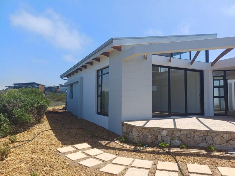 A modern exterior view of the property featuring a stone-clad patio, large sliding glass doors, and timber roof rafters.