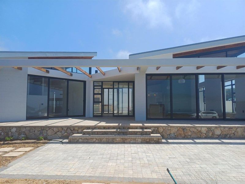 Modern rear exterior featuring a spacious paved patio, stone-clad retaining wall, timber pergola, and large floor-to-ceiling glass sliding doors.