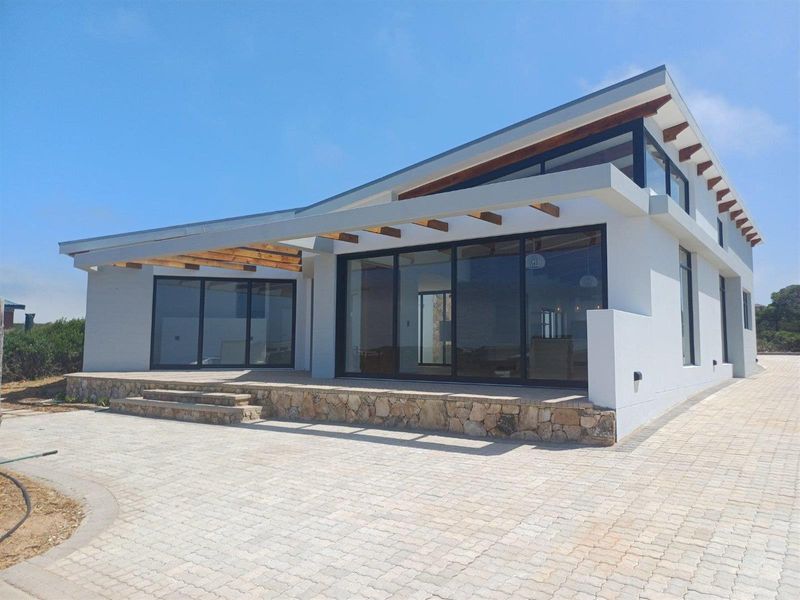 Modern rear exterior view featuring a stone-clad patio, large sliding glass doors, and exposed timber rafters under a contemporary mono-pitch roof design.