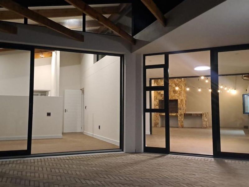 A spacious open-plan living area featuring large sliding glass doors, exposed timber ceiling beams, and a stone-clad built-in fireplace.