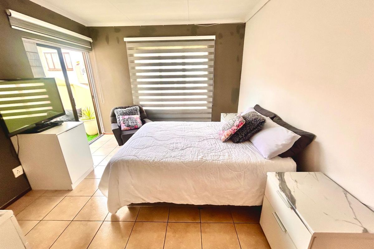 A bedroom featuring tiled flooring, dual-tone wall finishes, and sliding glass doors providing access to an outdoor area with fitted roller blinds.