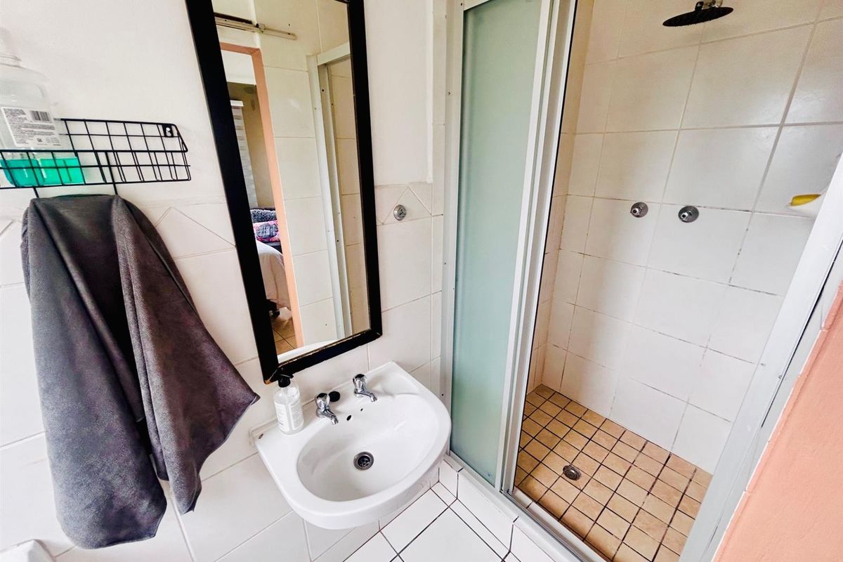 Compact bathroom featuring a wall-mounted basin, a framed mirror, and a tiled shower enclosure with a glass sliding door.