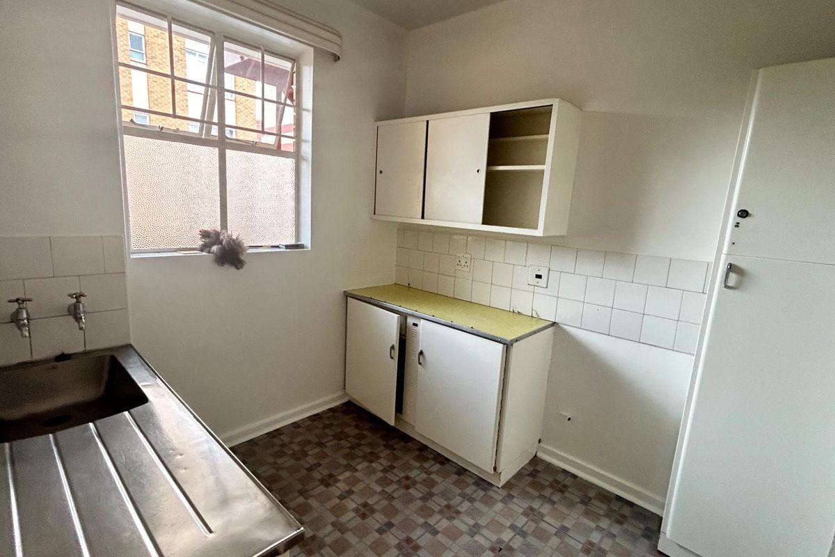 A compact, dated kitchen featuring a stainless steel sink, basic cabinetry, tiled splashbacks, and original flooring, offering potential for a modern renovation.