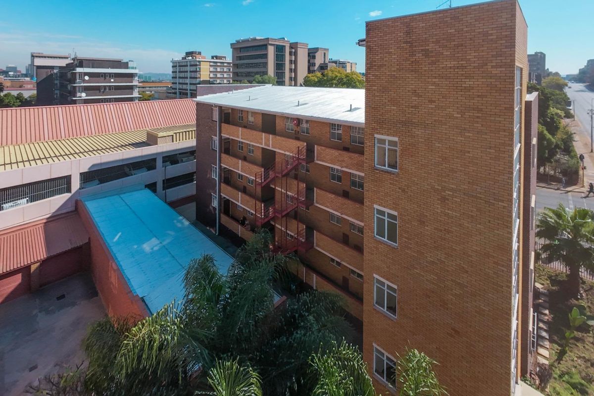Aerial view of a multi-story brick commercial building featuring external metal staircases and a metal roof structure in an urban setting.