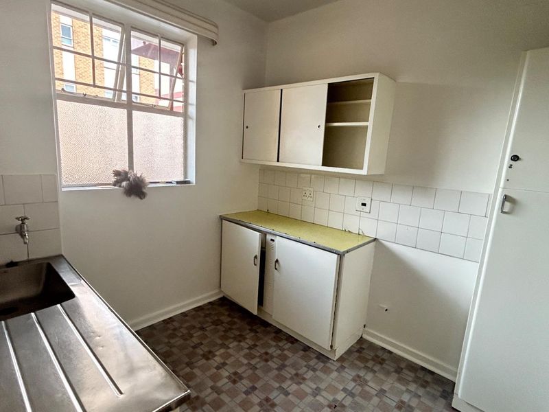 A compact, dated kitchen featuring a stainless steel sink, basic cabinetry, tiled splashbacks, and original flooring, offering potential for a modern renovation.