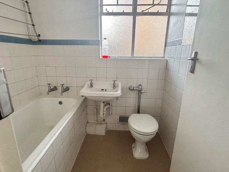 A dated bathroom featuring a standard bathtub, wall-mounted basin, and toilet with white tiled walls and a frosted glass window.
