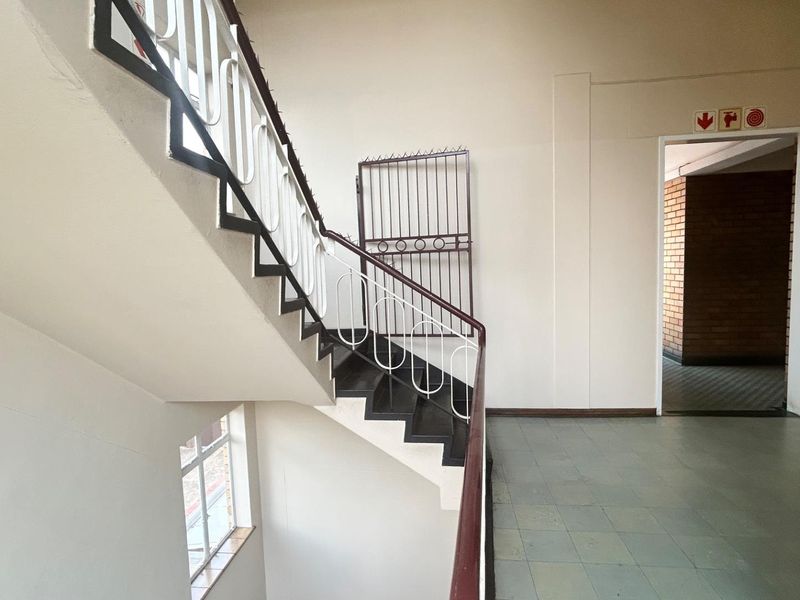 A functional commercial stairwell featuring a metal staircase with a security gate and tiled flooring leading to an adjacent room.
