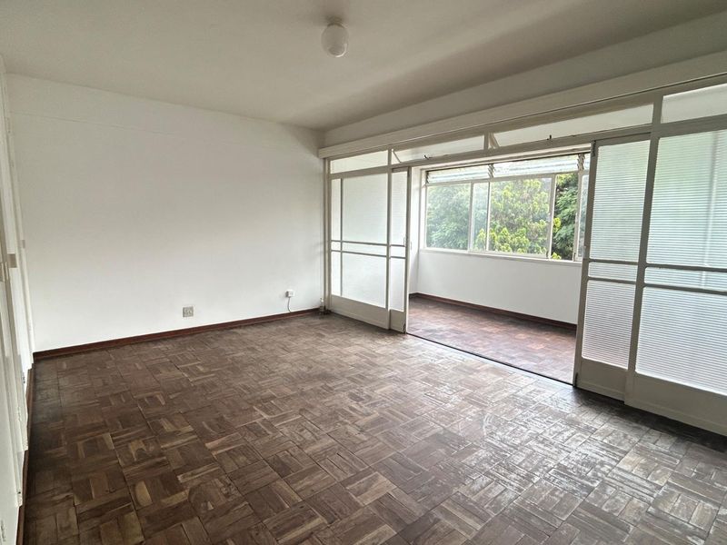 Spacious living area featuring classic parquet flooring and large sliding glass doors that open onto an enclosed balcony, providing ample natural light.
