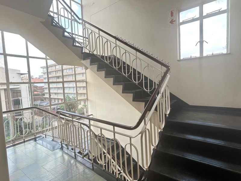A commercial stairwell featuring metal railings, large windows providing natural light, and tiled flooring, connecting multiple levels of the building.