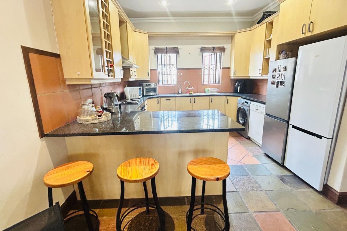 A functional kitchen featuring light wood cabinetry, granite countertops, a breakfast bar, and integrated space for laundry appliances.