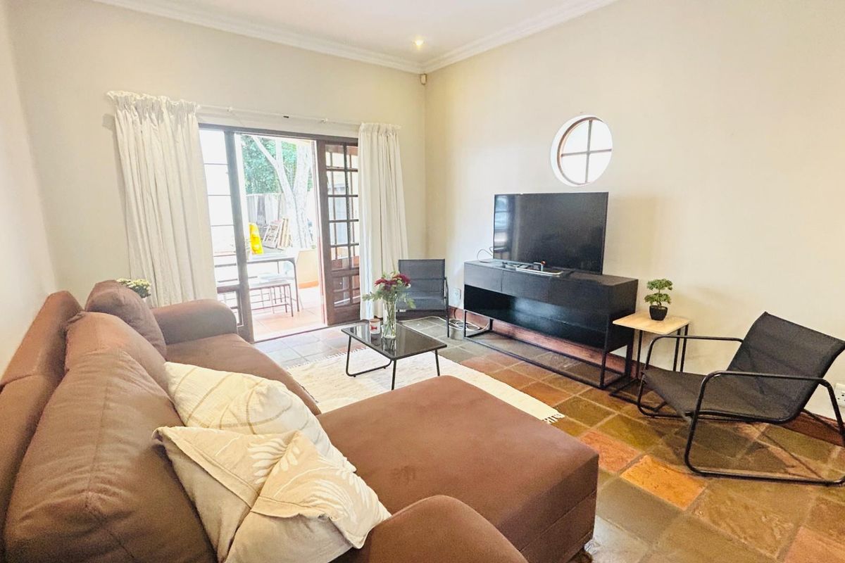A comfortable living room featuring terracotta floor tiles, a circular accent window, and sliding glass doors providing direct access to an outdoor patio area.
