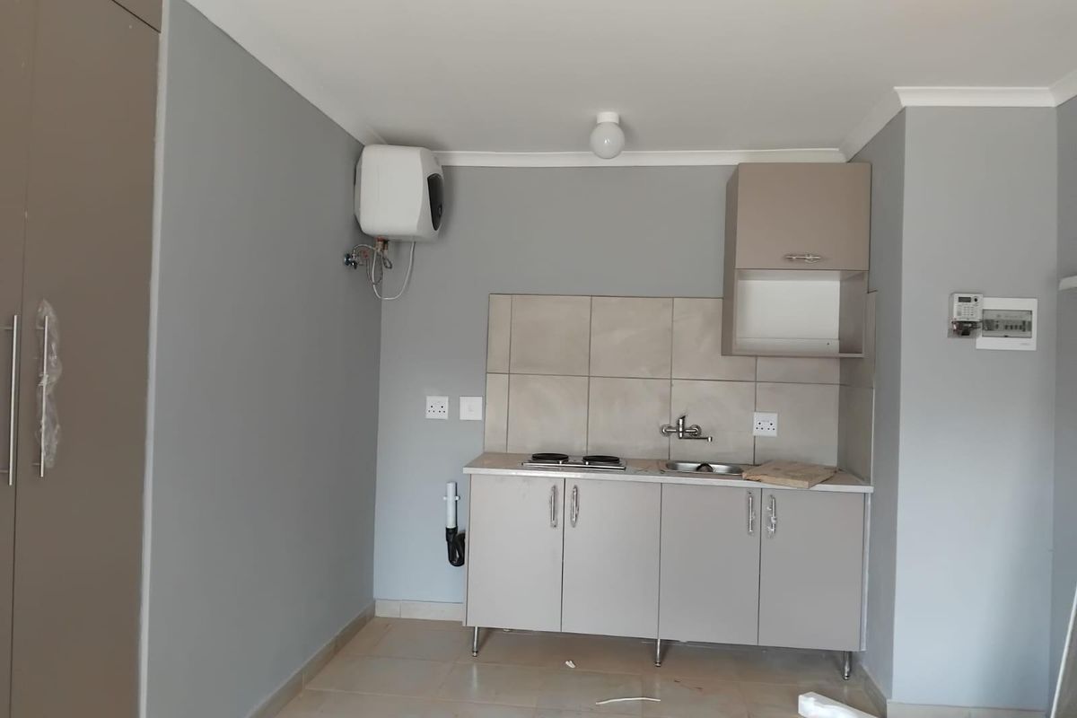 A compact, modern kitchenette featuring built-in cabinetry, a sink, a hob, and a wall-mounted electric water heater in a neutral grey finish.