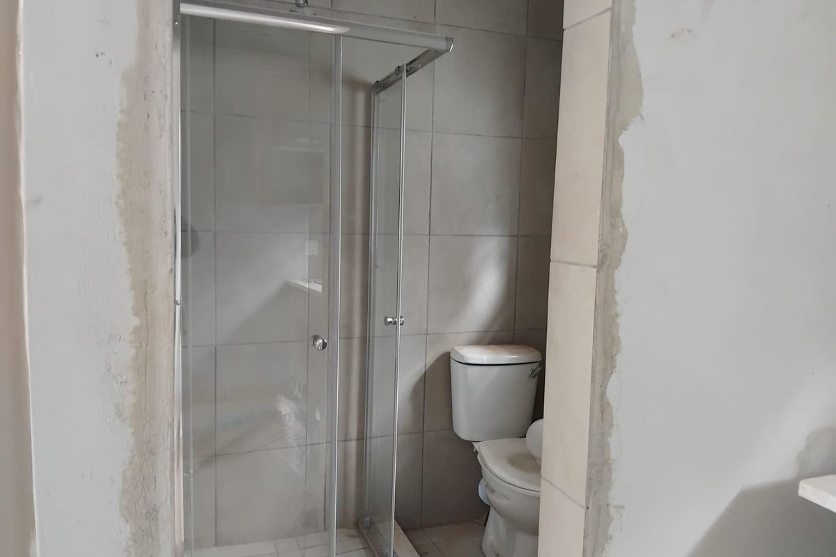 A bathroom in the process of renovation, featuring a glass shower enclosure and toilet, with unfinished wall plastering around the entrance.