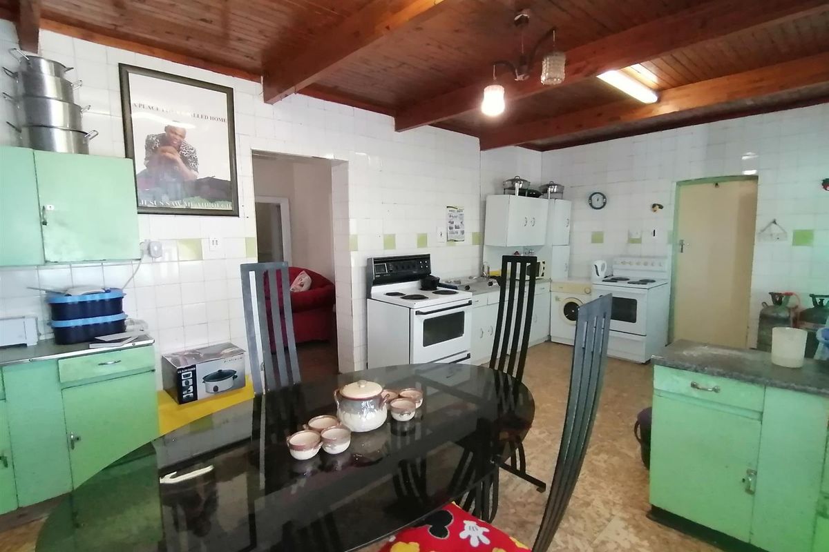 A dated kitchen featuring original cabinetry, tiled walls, and exposed timber ceiling beams, offering a functional layout with space for a dining area.