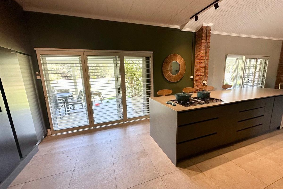 Modern kitchen featuring a large central island with a built-in gas hob, tiled flooring, and sliding glass doors opening to an outdoor patio area.