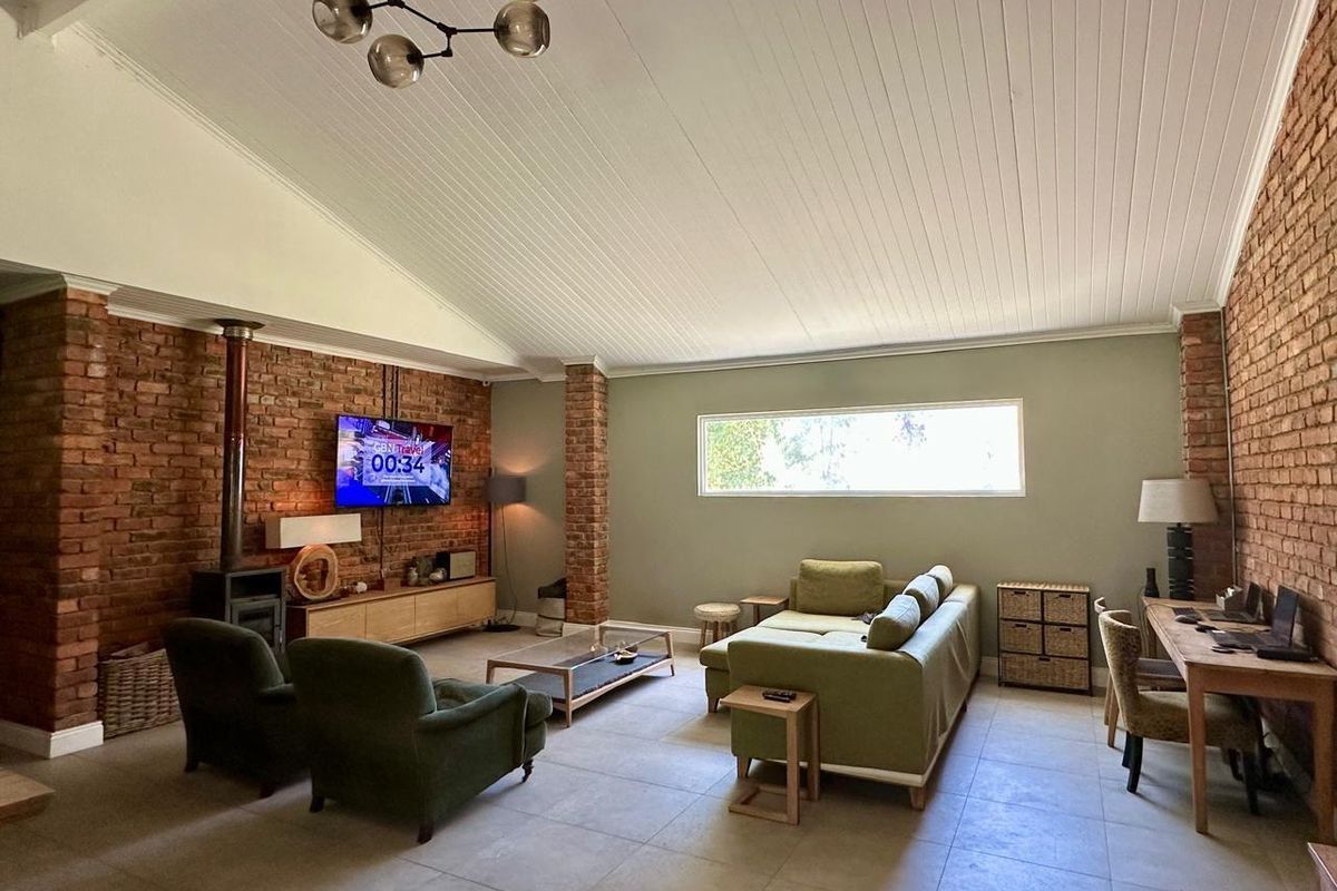 Spacious living room featuring exposed brick walls, a high vaulted timber ceiling, tiled flooring, and a built-in wood-burning fireplace.
